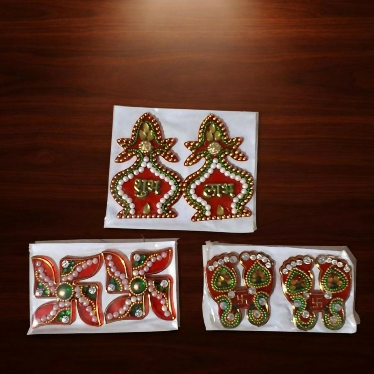 Three individually packaged sets of Shubh Labh, Swastik, and Laxmi Charan Paduka stickers on a dark wooden surface.