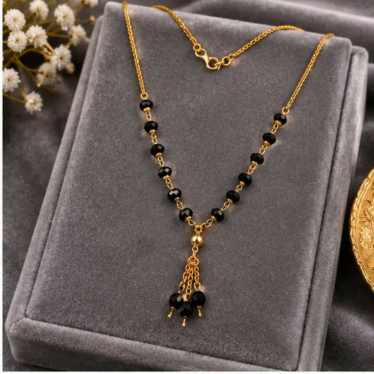 A gold chain necklace with black beads and a triple tassel pendant rests on a grey velvet display.