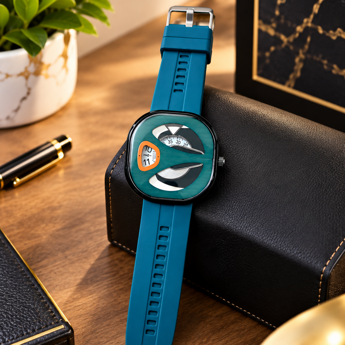 Green watch with a teal silicone band and unique dial, positioned on a black leather box with a pen nearby.