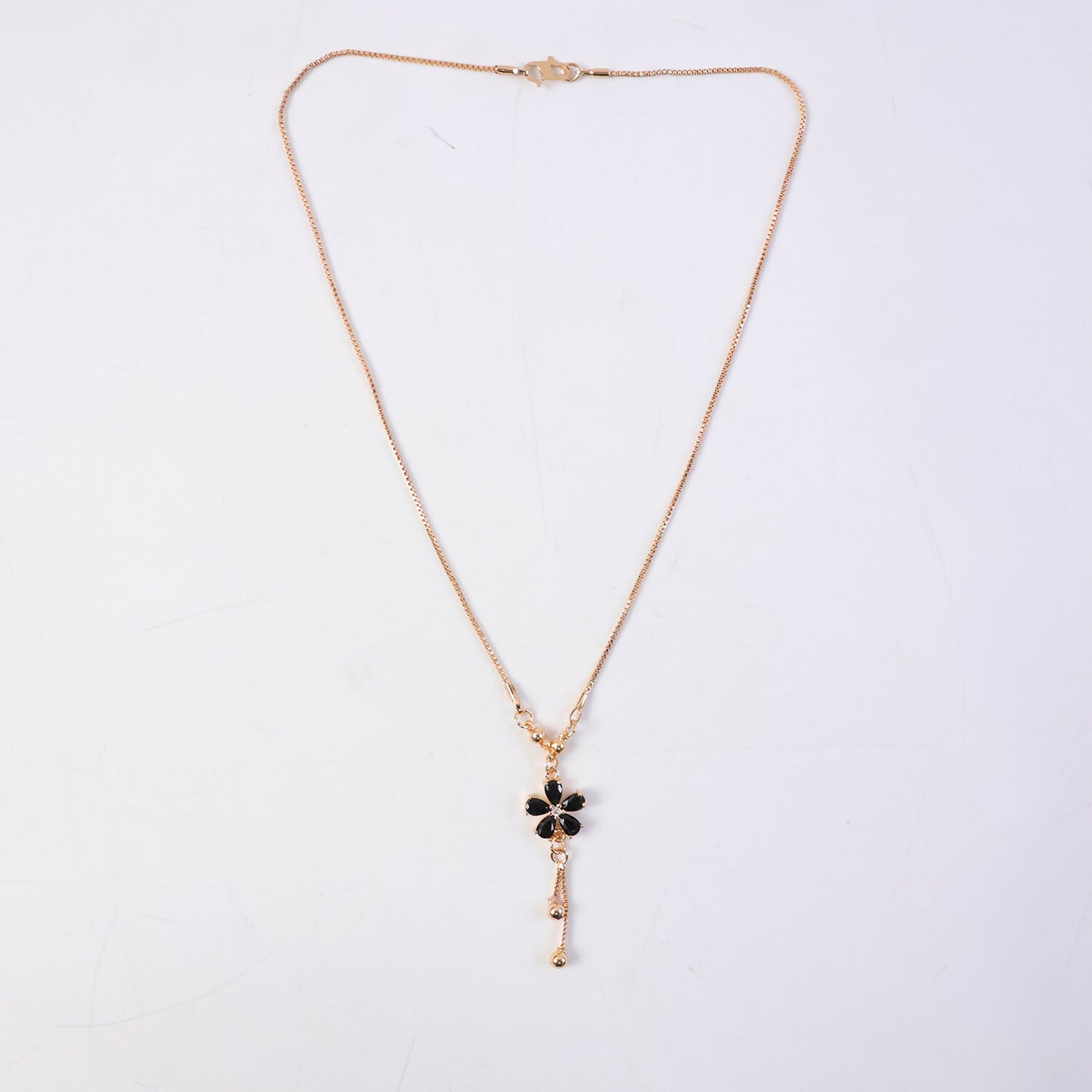 Gold finish necklace featuring black floral pendant with stones and hanging drop