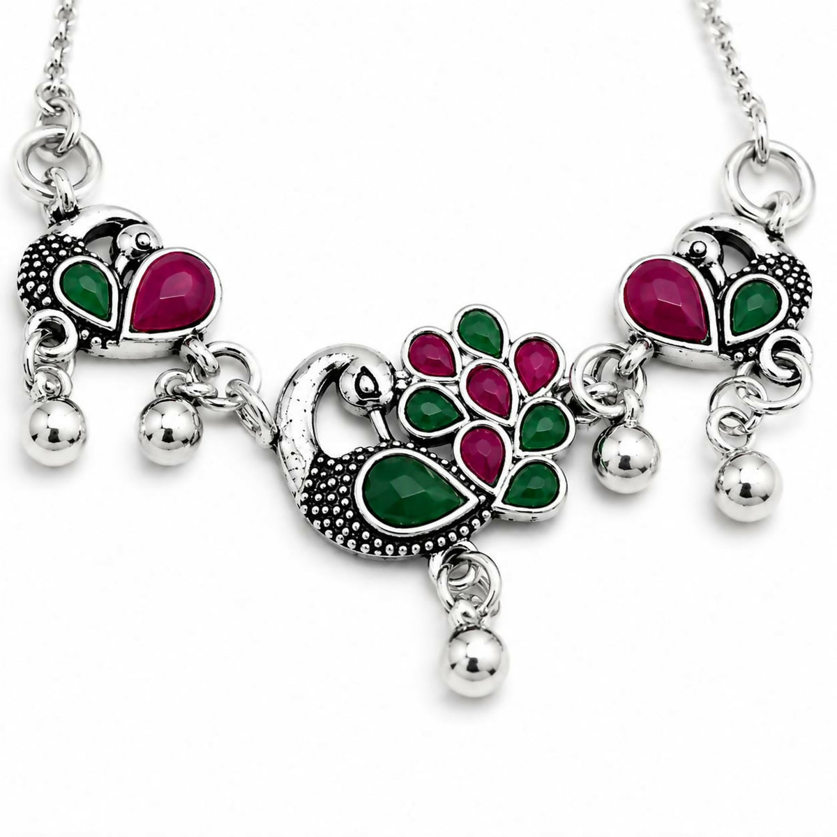 Close-up of silver bolo bracelet with ruby and emerald peacock motifs and small dangling beads.