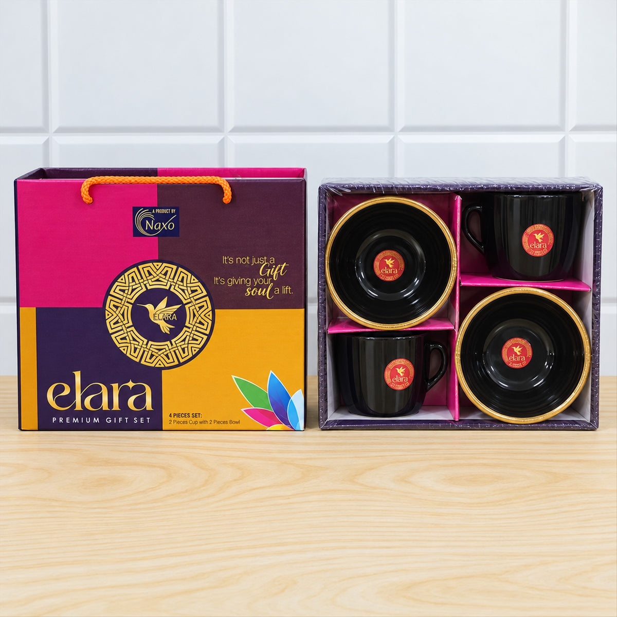A colorful gift box and a purple box containing two black ceramic mugs and two bowls with gold rims.