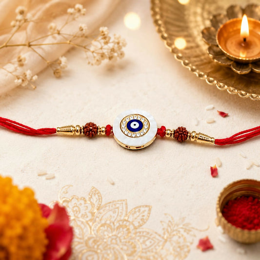 A red thread bracelet with a white evil eye dial, gold accents, and brown beads lies on an embroidered cloth with a lit diya.