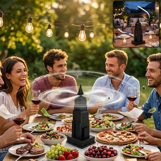 A black Empire State Building-shaped fly repeller fan sits on a wooden table surrounded by four smiling people eating dinner