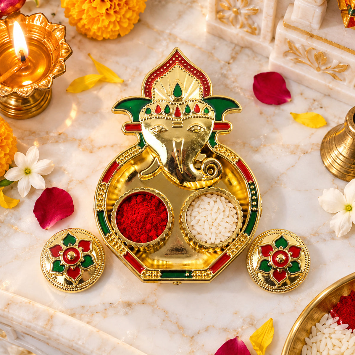 A golden Ganesha-shaped kumkum holder with red powder and white rice on a marble surface, surrounded by flowers and a lit