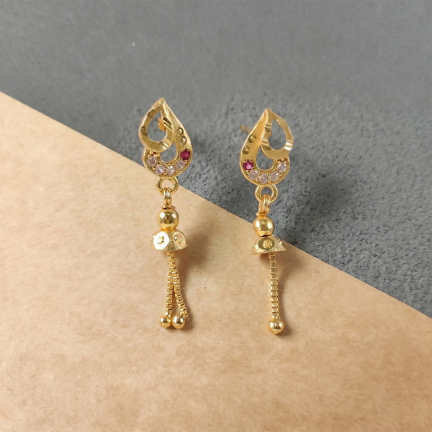 Close-up of gold polished dangler earrings showcasing diamond and ruby detailing