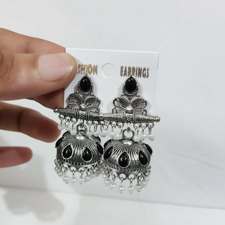 A hand holds the oxidized silver jhumka earrings with black stones and white pearls on a white