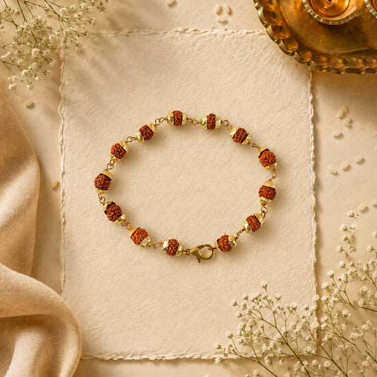 A gold-plated chain bracelet with rudraksha beads and a clasp on a cream paper with baby's breath flowers.