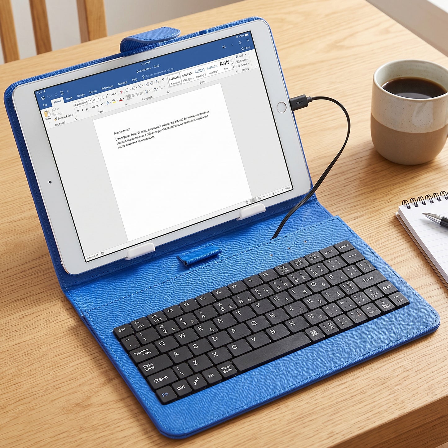A blue PU leather case with a tablet and wired keyboard sits on a wooden table next to a coffee mug.