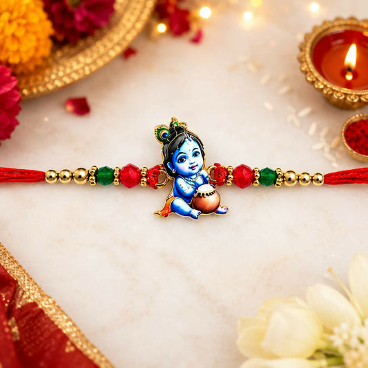 A red thread with a blue Bal Krishna charm, flanked by gold, red, and green beads, rests on a marble surface with festive