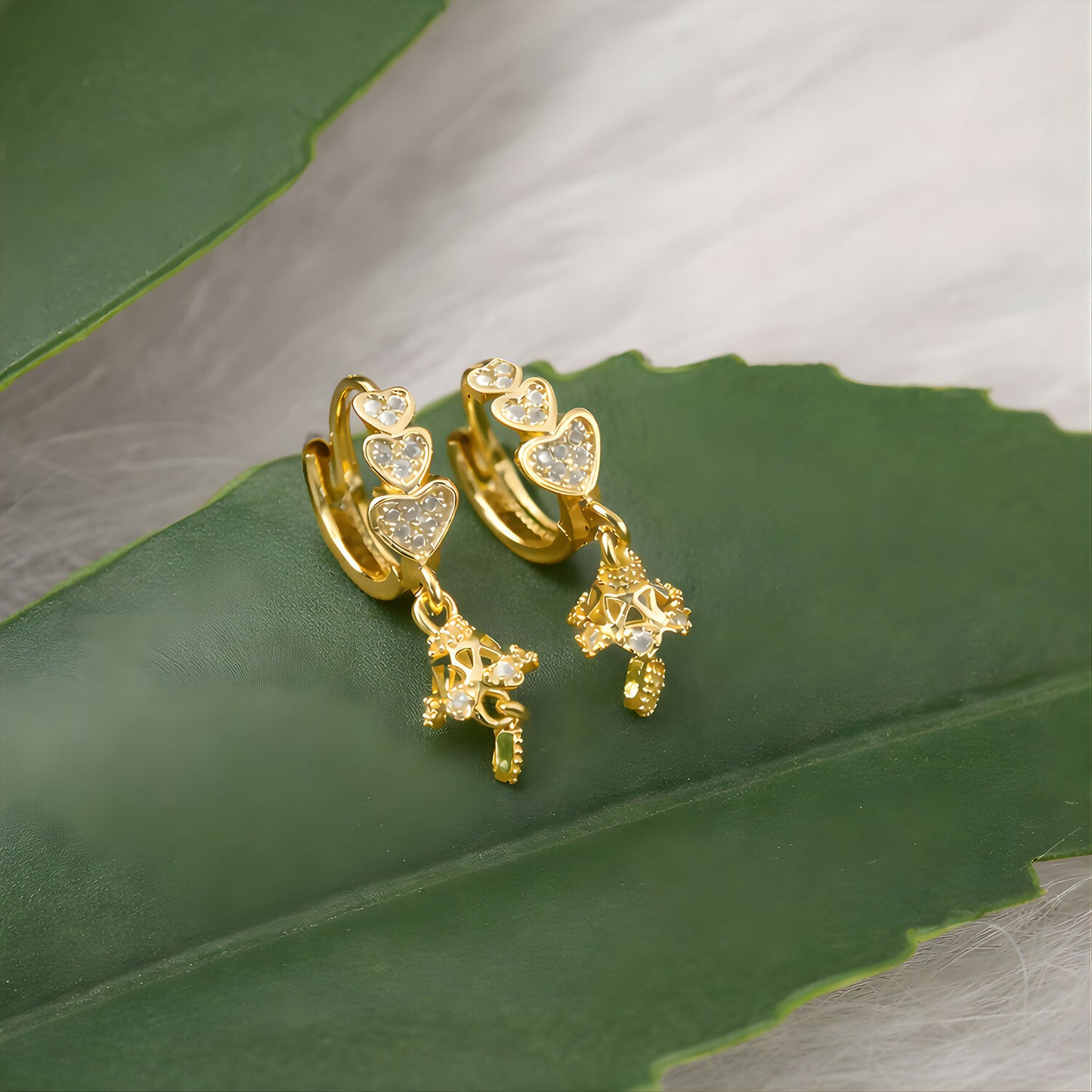 Front view of triple heart drop earrings with sparkling stone accents and gold finish