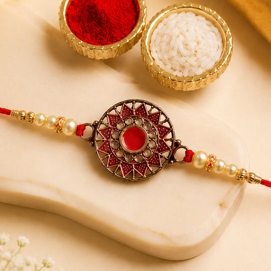 Traditional Rakhi with red centre stone and pearl beads, showcasing gold detailing for Raksha Bandhan.