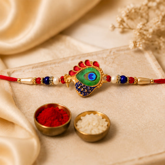 Golden peacock feather rakhi with enamel, pearls, and beads on a red thread.
