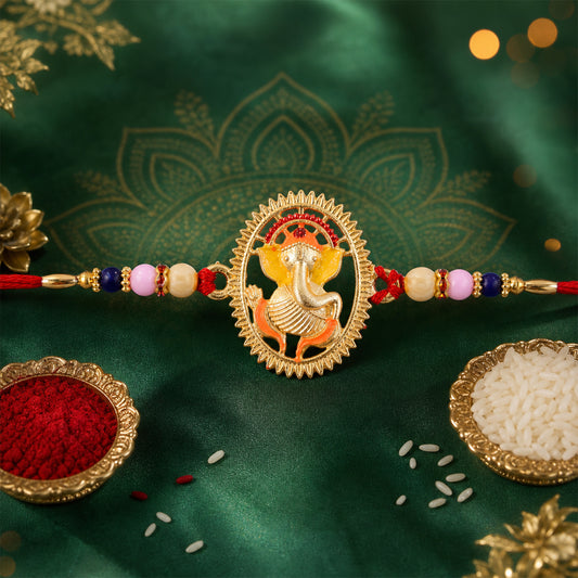A golden Ganesha charm with red, orange, and yellow enamel sits on a red thread with colorful beads, against a green