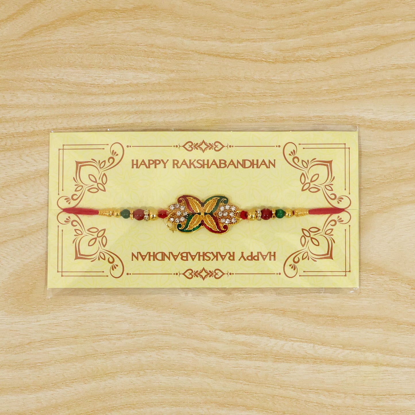 A red thread bracelet with a golden, red, and green flower motif is displayed on a yellow