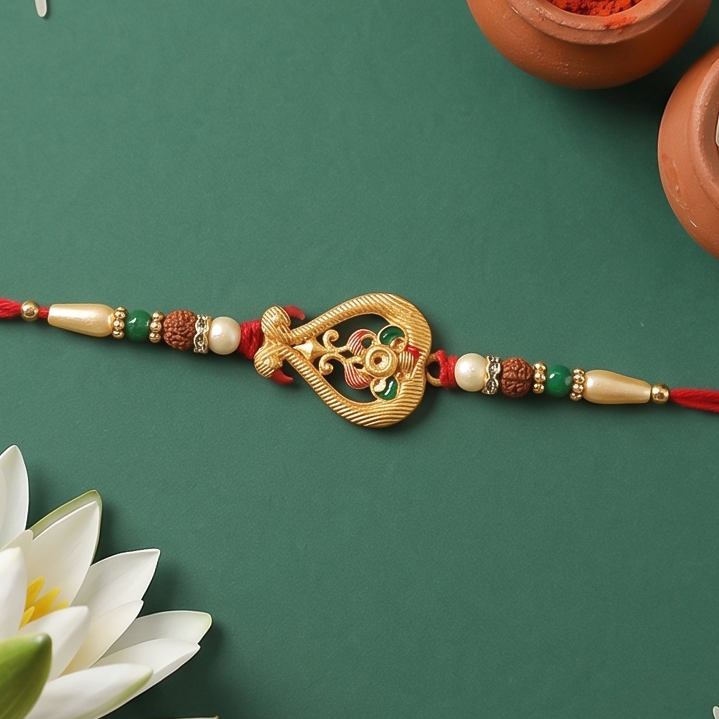 A red thread bracelet featuring a gold-toned, intricate centerpiece with colorful enamel, flanked by various beads, on a