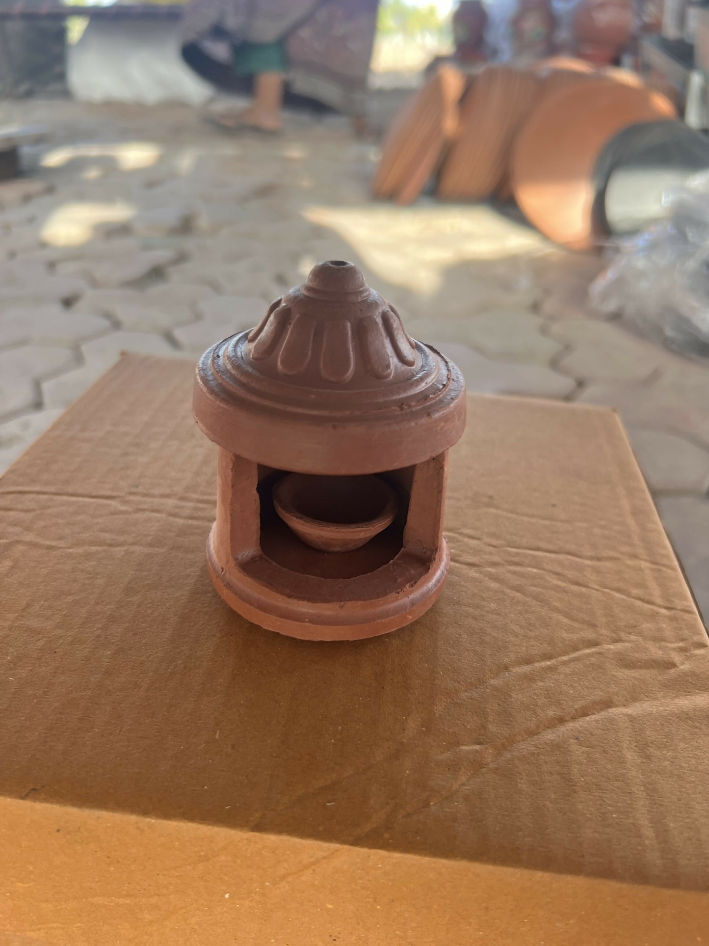 Decorative terracotta diya with protective hut cover in warm brown