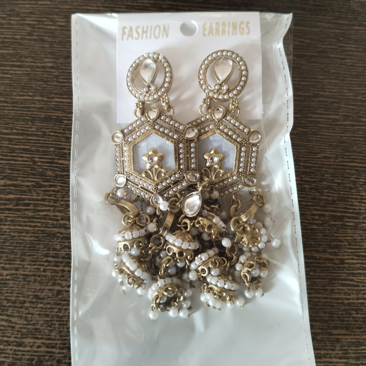 A pair of gold-toned hexagonal earrings with white enamel, clear stones, and small white pearls in clear plastic packaging.