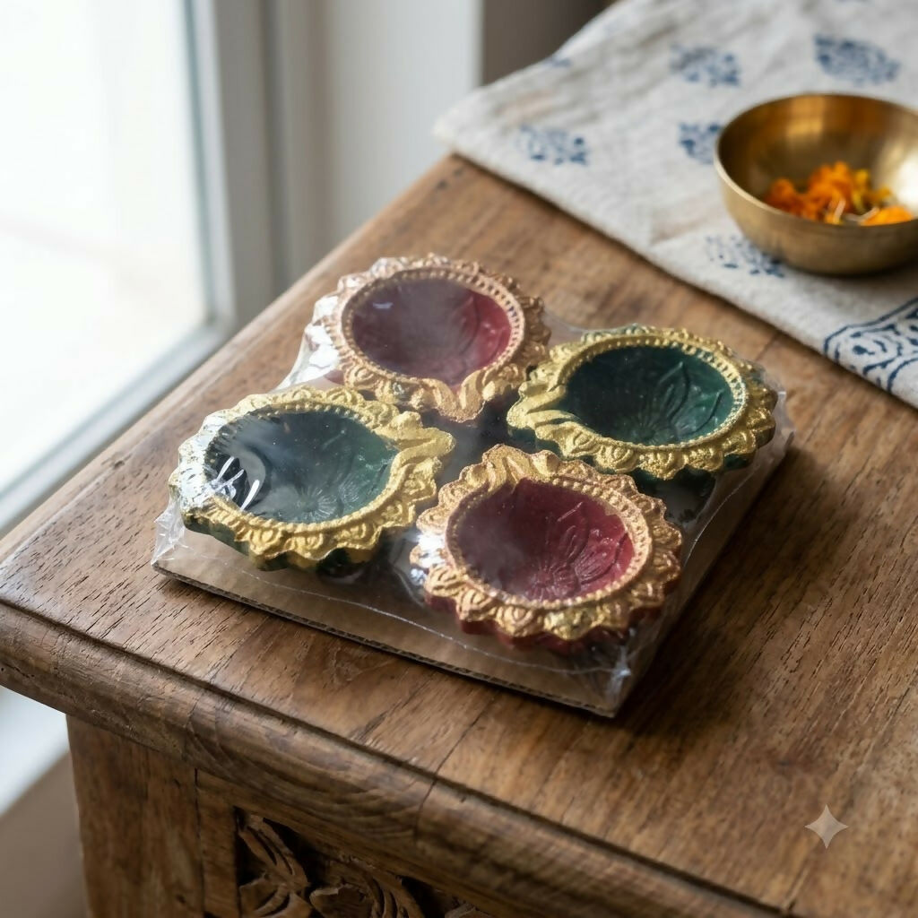 Four packaged diyas, two red and two green, sit on a rustic wooden table next to a small brass bowl.