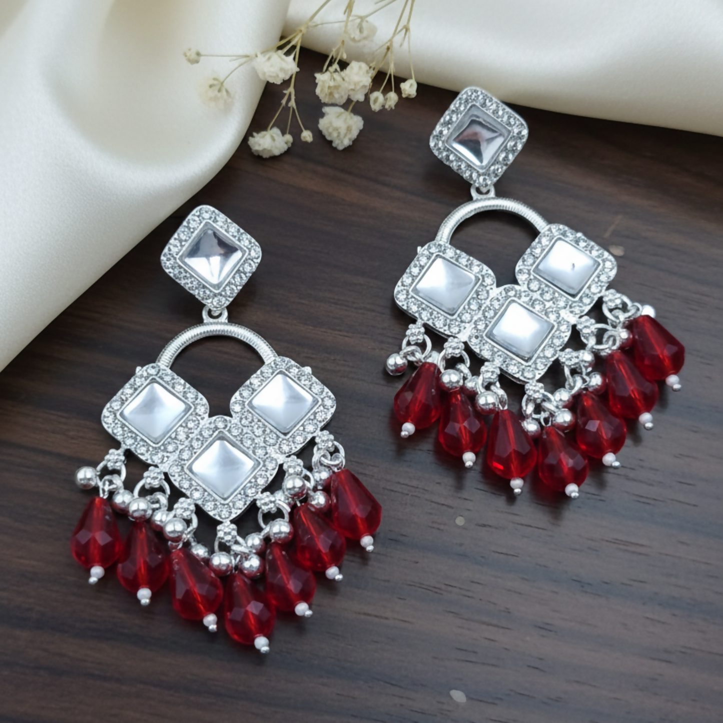 Close-up image of silver plated earrings with sparkling square crystals and red beads