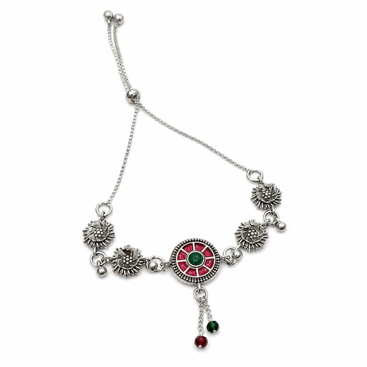 The oxidized silver bracelet, featuring a red and green enamel mandala and floral links, is laid flat on a white background.