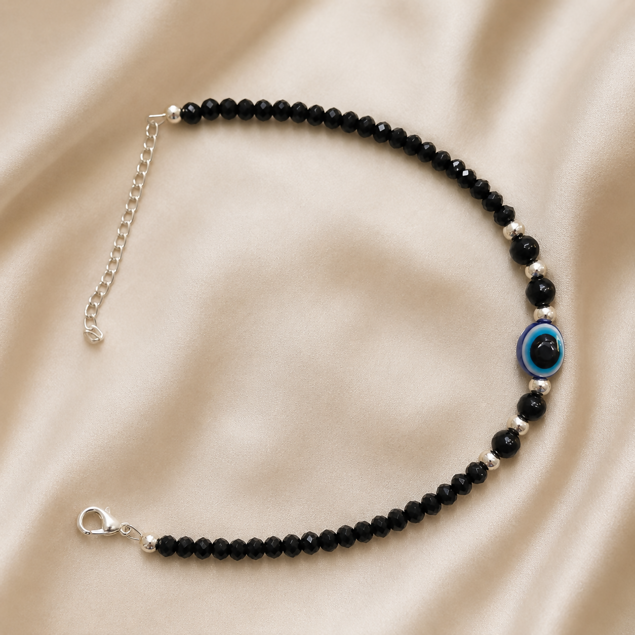 Black evil eye beaded anklet pair with a blue charm on a white background.
