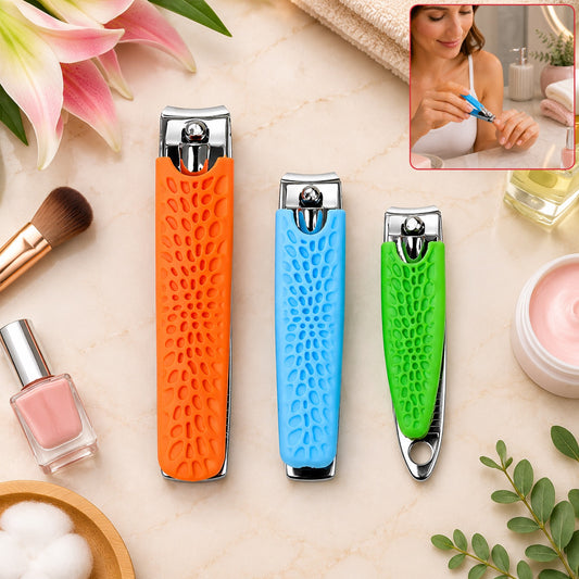 Three stainless steel nail clippers with orange, blue, and green textured silicone handles on a vanity with cosmetics.