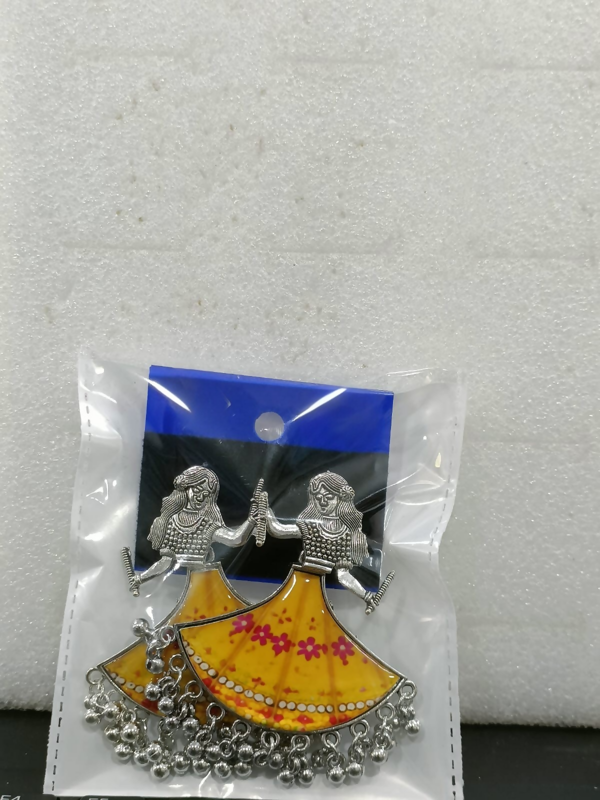 The pair of Dandiya girl earrings is packaged in a clear plastic bag with a blue backing card.