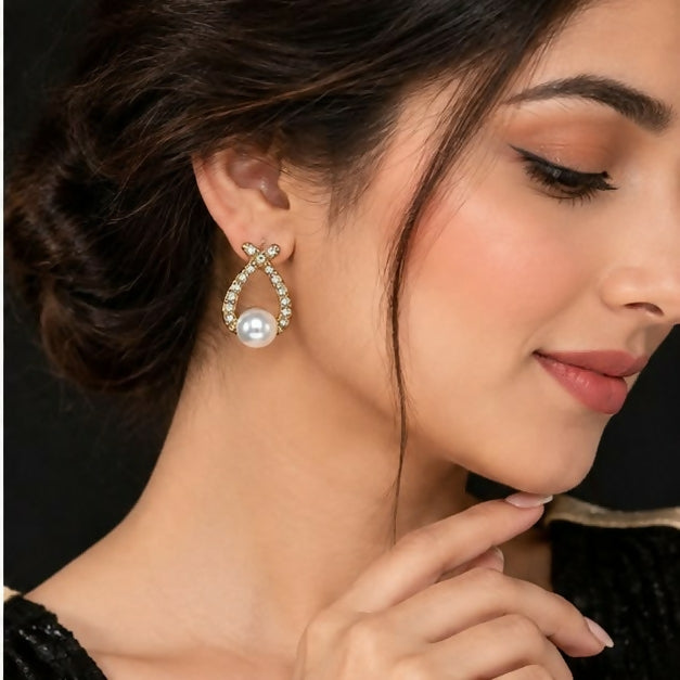 Close-up of a single gold-tone teardrop earring showing clear stone detailing and pearl bead