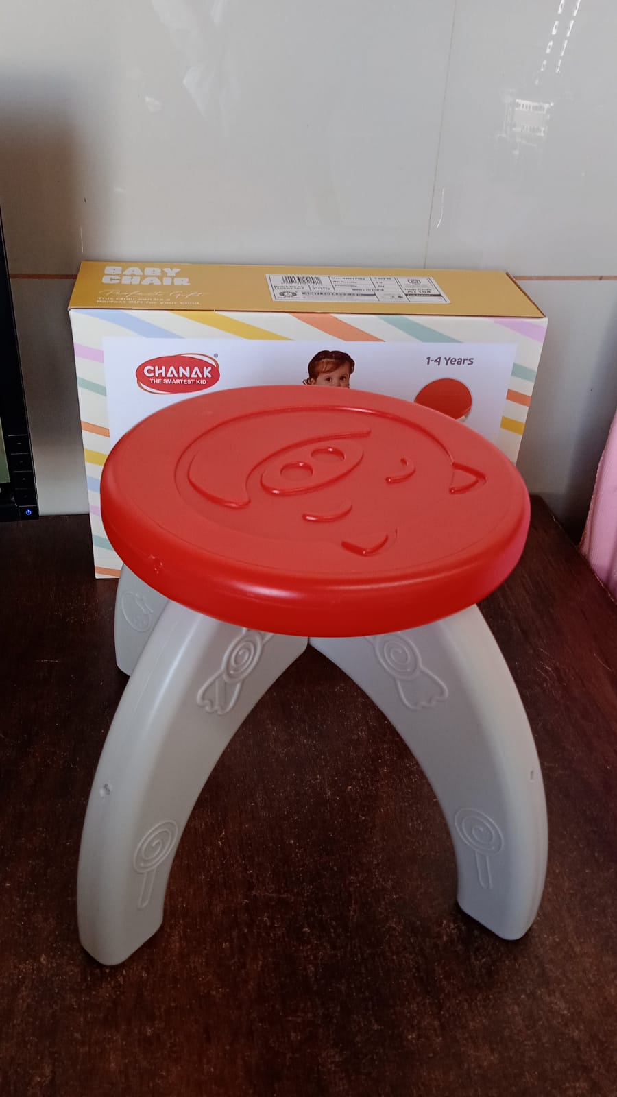 A red and white plastic stool with a pig face on top sits in front of its product box.