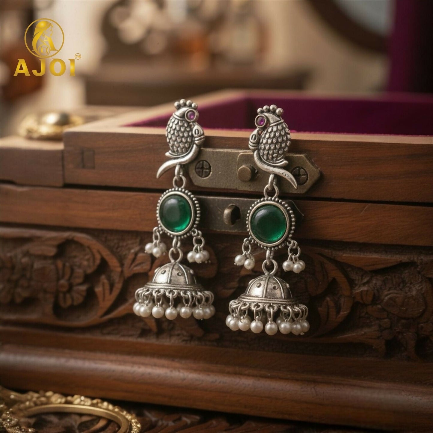 Close-up of peacock motif on antique silver jhumka earrings with emerald green stone