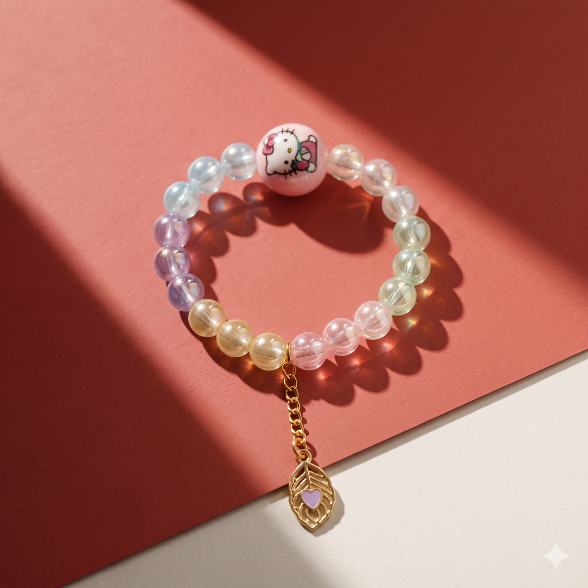 A single pastel beaded bracelet with a pink Hello Kitty bead and a gold leaf charm on a pink background.