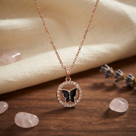 Rose gold chain with a circular pendant featuring a black butterfly surrounded by small clear stones.