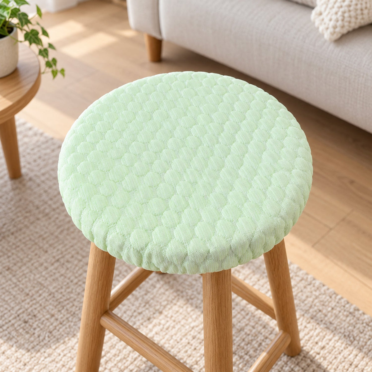 Light green textured round stool cushion cover on a wooden stool in a living room setting.