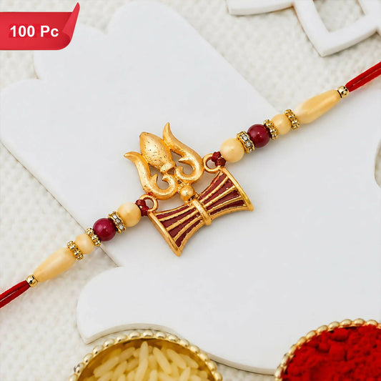 A gold and red Shiva Trishul Rakhi with a damaru drum and trident symbol, flanked by cream, red, and gold beads on a red