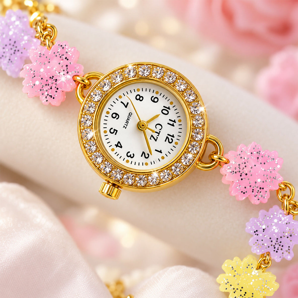 Close-up of the gold-toned watch face with a rhinestone-encrusted bezel and pastel glitter flower links.