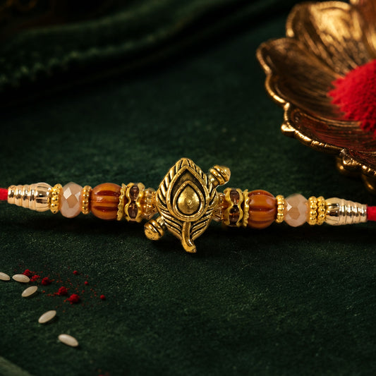 Close-up of Peacock Paisley Golden Rakhi with blue-green enamel and pearl accents