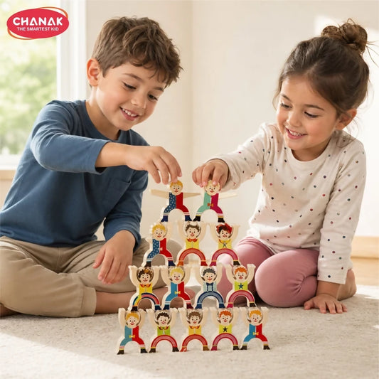 Two children happily stack colorful wooden clown figures to form a pyramid on a light carpeted floor.