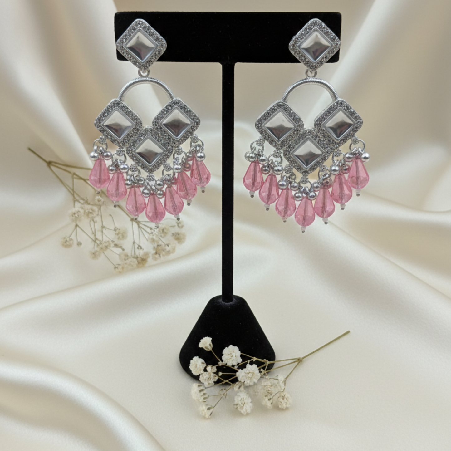 Close-up of silver plated earrings with square-cut crystals and pink beads