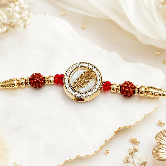 Golden feather dial with crystal halo and rudraksha accents on a white textured surface with delicate white flowers.