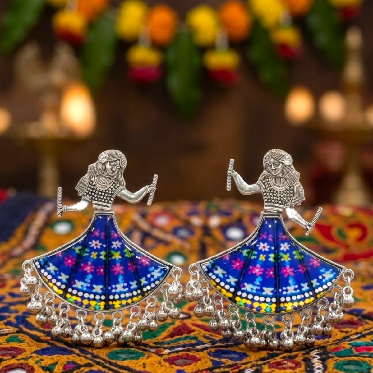 Pair of oxidized silver dancing doll earrings with blue floral skirts on a colorful patterned fabric.