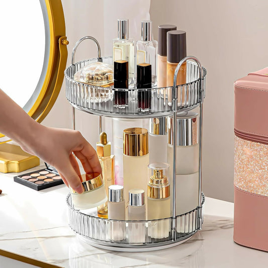 A hand reaches for a cream jar on a clear two-tier rotating organizer filled with various cosmetic bottles on a white vanity.