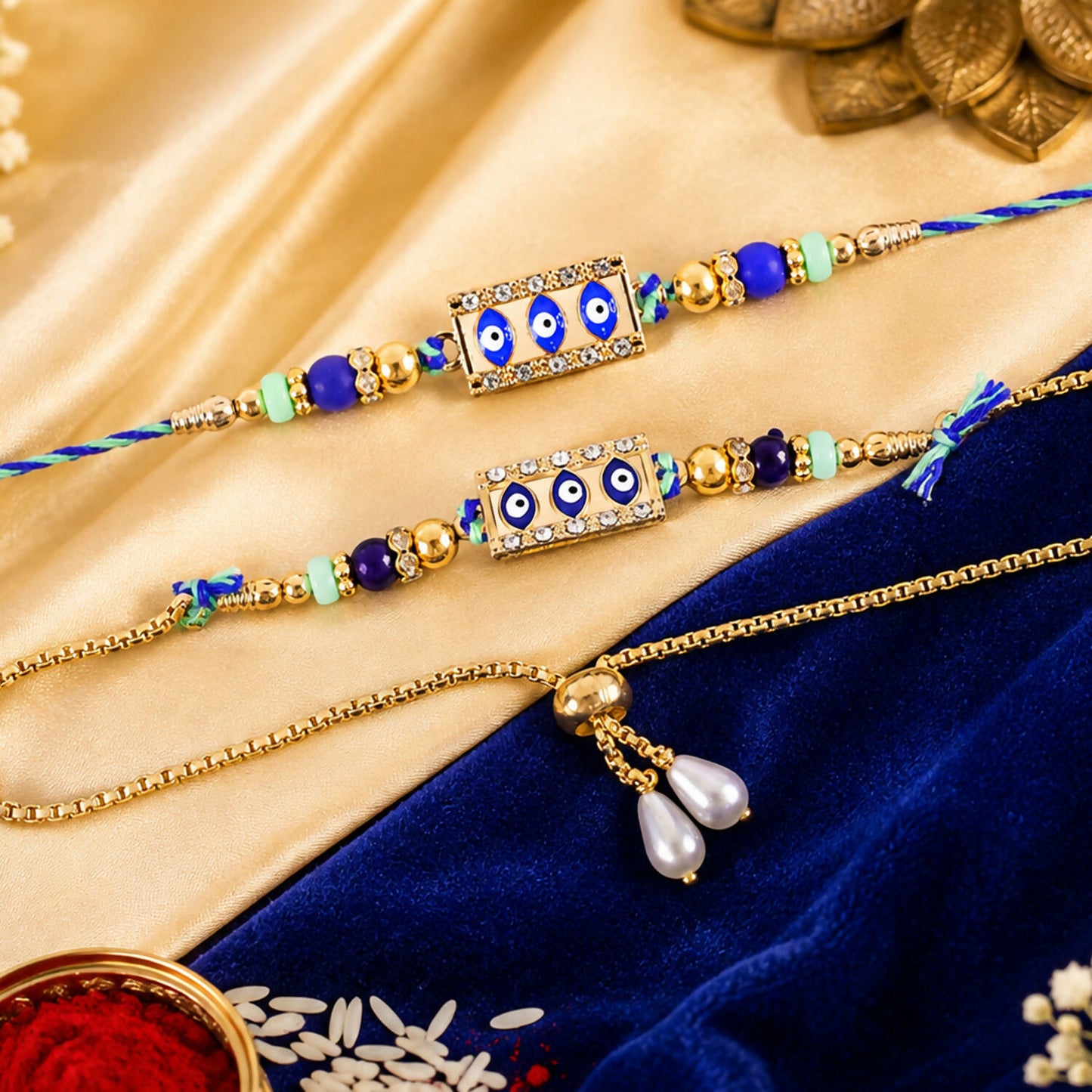 Two blue and gold evil eye rakhis, one a bracelet, on a gold and blue fabric with rice.