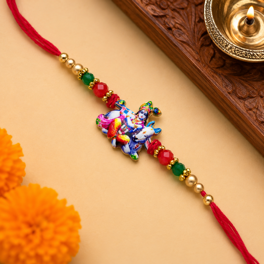 A red thread with a colorful Bal Gopal Krishna and cow charm, flanked by red, green, and gold beads, lies on a light brown