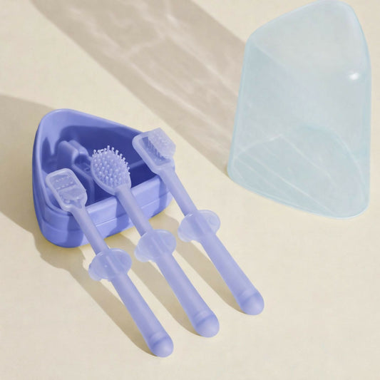 Three purple silicone baby toothbrushes with different head types in a lavender holder, next to a translucent light blue