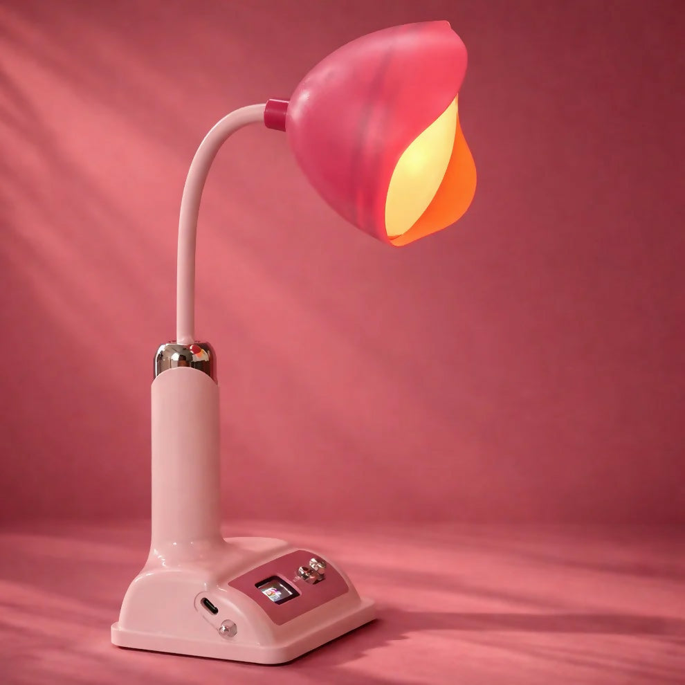 A pink desk lamp with a flower-shaped shade emitting a warm glow is shown against a dark pink backdrop.