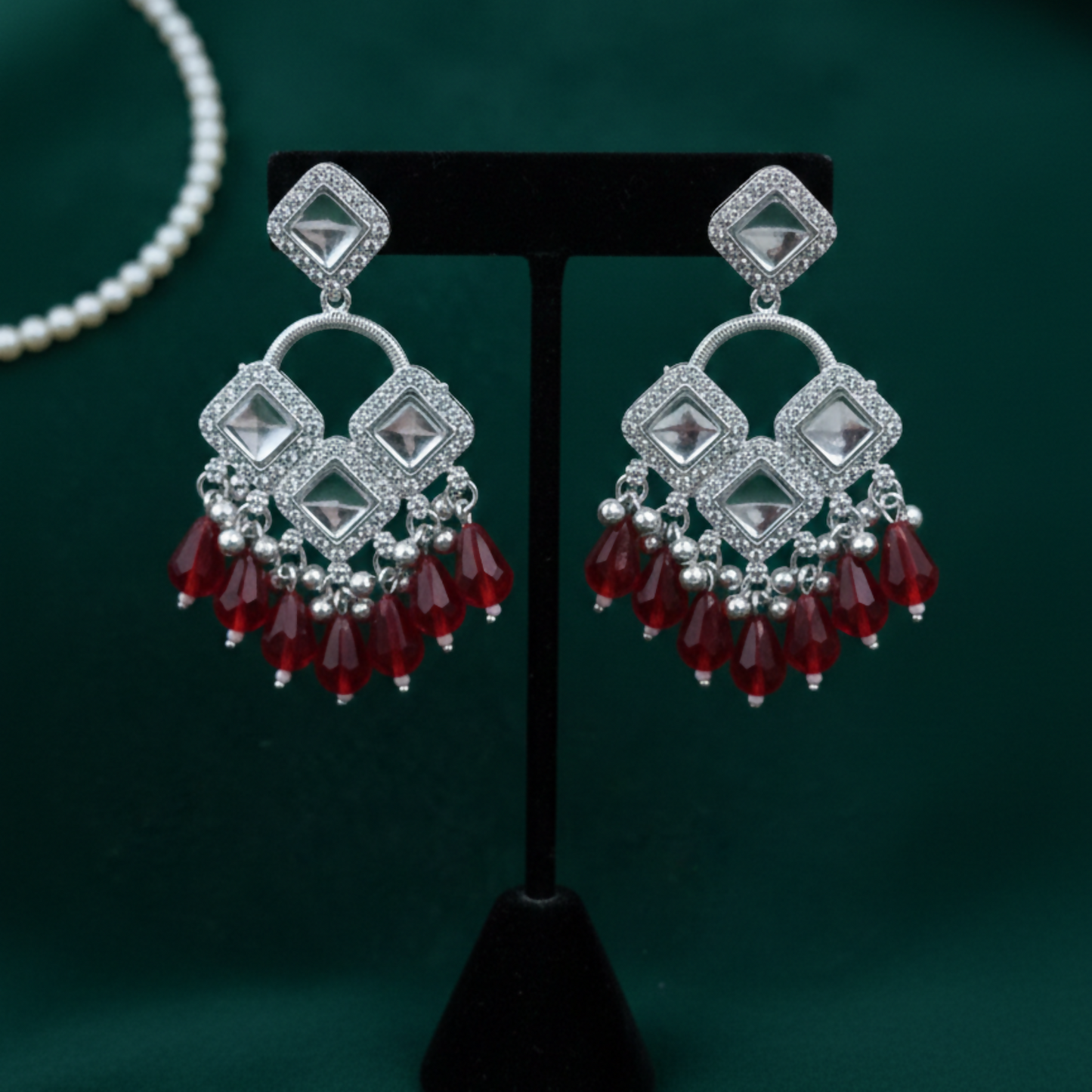 Silver plated earrings hanging on jewelry stand displaying square crystals and red teardrop beads