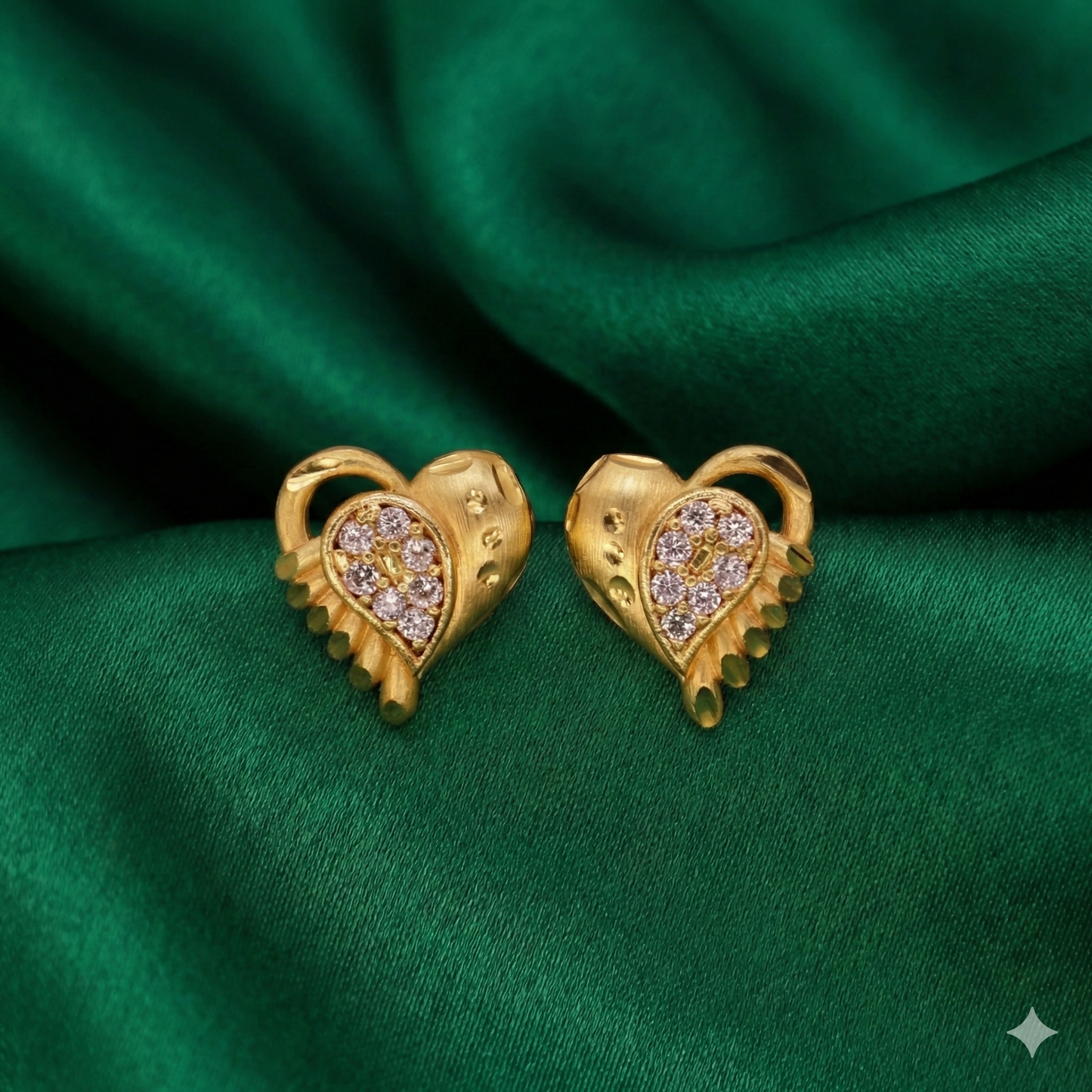 Gold heart stud earrings with textured matte gold and white crystals on maroon background