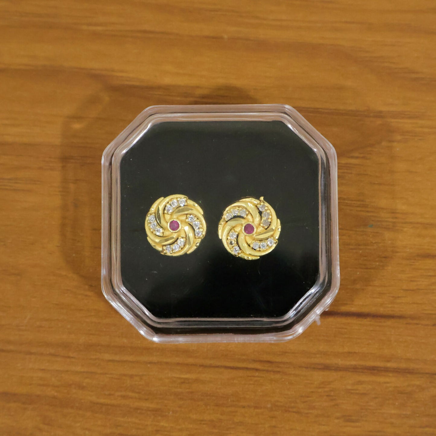 Detailed view of gold spiral stud earrings with sparkling red stones