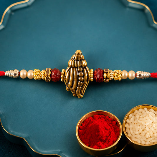 Close up of Shankh Conch Devotional Rakhi with golden work, pearl beads, and red accents.